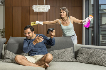 Wall Mural - arab man playing a video game while woman is cleaning around him