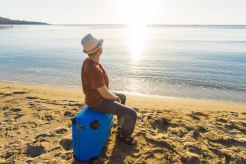 Young man holding luggage at the sea. Travel, summertime, holidays and people concept.