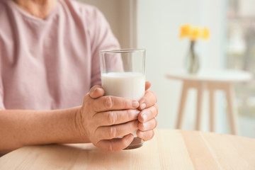 Poster - Old woman holding glass with fresh milk at table, closeup