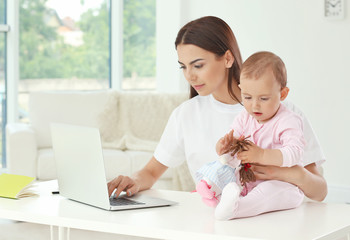 Wall Mural - Young mother holding baby while working in home office