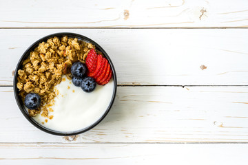 bowl of granola with yogurt, fresh berries, strawberry on wood table.