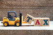 Toy plastic forklift hold block T to compose and fulfill wording TAX on wood background