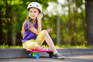 Wall Mural - Pretty little girl learning to skateboard on beautiful summer day in a park. Child enjoying skateboarding ride outdoors.