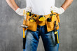 © smspsy - unknown handyman with hands on waist and tool belt with construction tools against grey background. DIY tools and manual work concept