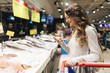 © santypan - Beautiful woman buying fish in supermarket while using her mobile.