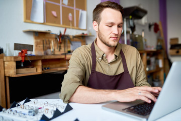 Portrait of young man using computer cataloging jewelry while appraising goods in pawn shop