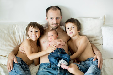 Wall Mural - Father of three boys, preschool, toddler and newborn baby, sitting in bed