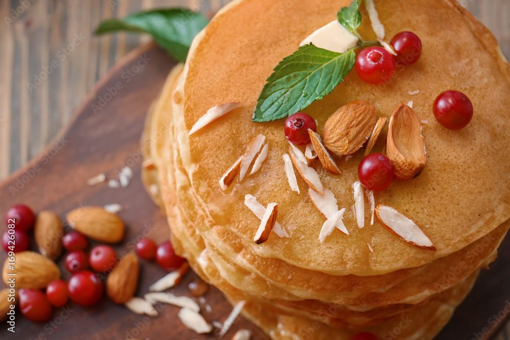 Delicious pancakes with nuts and berries on wooden board