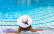 © moofushi - Elegante Frau mit weißem Hut sitzt am Rande eines Pools und entspannt