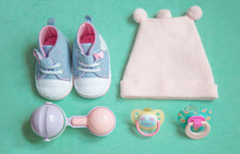 Baby Stuff Is On A Blue Background. Top View Closeup. Things Little Girl, Pacifier, Rattle, Hat, And Shoes.newborn Baby Necessities