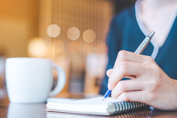 Business woman hand is on a notepad with a pen on a wooden desk in the office