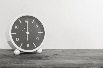 Closeup alarm clock for decorate in 6 o'clock on old wood desk and white cement wall textured background in black and white tone with copy space