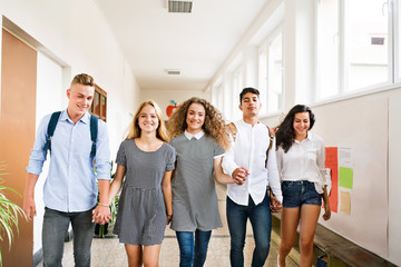 Teenage students walking in high school hall, holding hands.