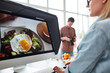 © pressmaster - Professional food designer retouching photo while sitting in front of modern computer, spacious production studio with panoramic windows on background