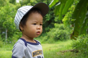 Attractive Asian toddler girl but look like toddler boy with white gap and grey body suit walk around garden with natural motion