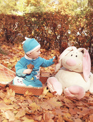  Little boy in nature sitting in open suitcase. Outings - the forest in autumn. Nearby are big hare toy 