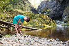 The Boy Is Standing On The Bank Of A Stream