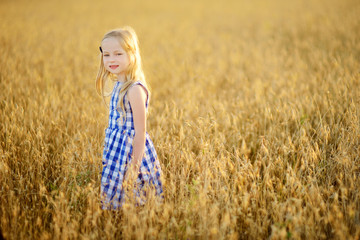 Wall Mural - Adorable girl walking happily in wheat field on warm and sunny summer evening