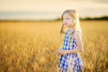 Wall Mural - Adorable girl walking happily in wheat field on warm and sunny summer evening