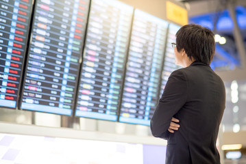 Young asian business man checking his flight from the flight information board in airport terminal 