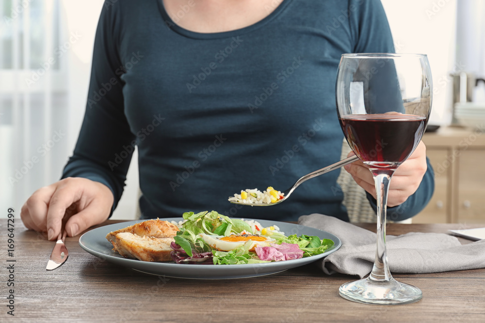 Woman eating tasty dinner and drinking wine in kitchen