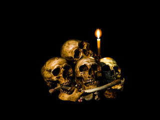 Wall Mural - Human skulls and pile bone with candle Light. Isolated on dark background with clipping path