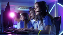 Beautiful Professional Gamer Girl And Her Team Participate In ESport Cyber Games Tournament. She Has Her Headphones And As A Team Leader She Commands Strategical Maneuvers Into Microphone.