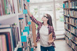 Side profile shot of young attractive girl student bookworm, studying in the ancient university`s library, searching information for her diploma on the book shelf, wearing casual outfit, spectacles