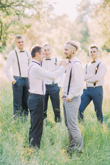 The best man is checking the wooden butterfly on the groom`s neck at the background of the best men in the green spring field.