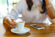 © yanadhorn - Asian business women hand holding espresso coffee in white cup with smartphone on the wooden table. business and coffee concept.