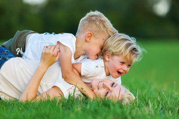 woman romps with her two sons on the grass