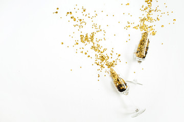 Champagne glasses with golden confetti tinsel on white background. Flat lay, top view celebrate party concept.