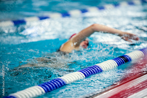 Plakat Obecnie nieostry kobiet pływak robi przedni indeksowania w konkursie. Anonimowy sportowiec w krytym basenie.