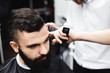 © nagaets - Master cuts hair and beard of men in the barbershop, hairdresser makes hairstyle for a young man