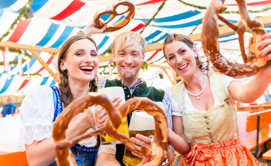 Wall Mural - Drei Freunde im Bierzelt auf Dult oder Oktoberfest halten Riesenbrezen in die Luft