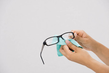 Glasses cleaning with fine microfiber cloth. Women hand cleaning glasses lens with blur green background.