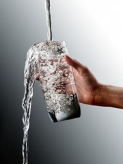 female hand with overflowing glass of water on grey gradation