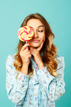 Young Pretty Smiley Woman Holding Lollipop In Hands Over Blue Background