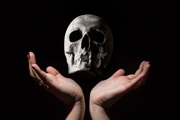 Wall Mural - Black magic concept. Human skull between woman hands on black background.