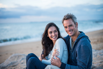 Poster - Beautiful couple sitting at the beach watching the sunset