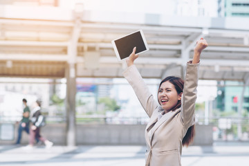 Successful business woman celebrating with arms up  and hands holding a tablet ,Happy with the success of the operation  eCommerce business .