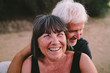 © Evgenij Yulkin/Stocksy - Couple of seniors sitting on the sand and smiling into the camera