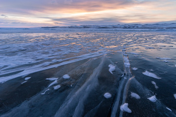 Wall Mural - ice of baikal lake with cracks and snow on sunrise. pink colorful sky.
