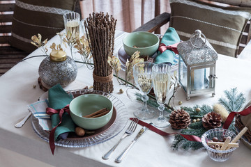 Holiday served table with tablecloth, wineglasses, plates, cones, candeles and sweets in restaurant. Festive table for two persons with champagne in glasses. Dinner party, winter style.