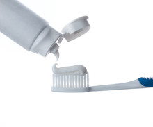 Toothpaste Being Squeezed Onto Toothbrush On A White Background