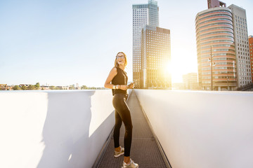 Wall Mural - Lifestyle portrait of a stylish woman walking on the modern bridge with skyscrapers on the background during the morning in Amsterdam city