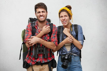 Wall Mural - Studio portrait of unhappy male and female tourists with backpack, camera and binoculars, scratching their hands with unhappy look after walk in deep forest. People, adventure, travelling concept