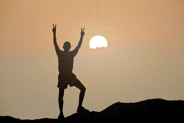 silhouette of man is climbing to peak of hill with sunset or sunrise background