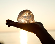Clear Quartz Skull On The Woman`s Open Palm In Front Of  The Rising Sun