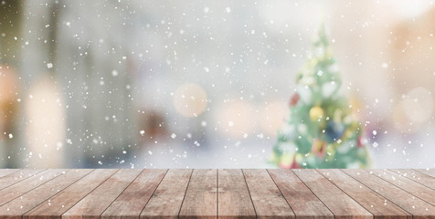 wood table top on blur with bokeh christmas tree background with snowfall - can be used for display 